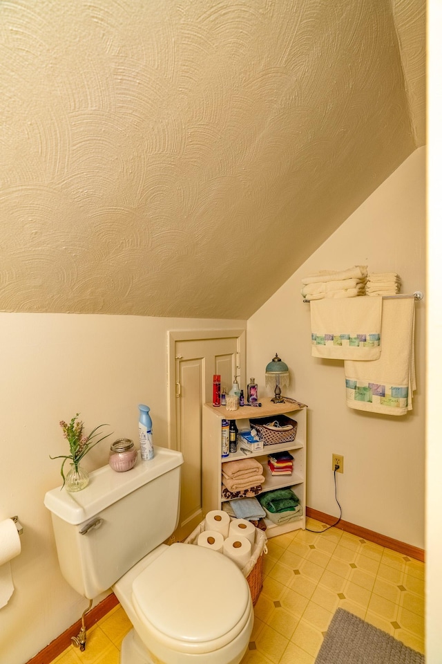 bathroom with vaulted ceiling, toilet, baseboards, tile patterned floors, and a textured ceiling