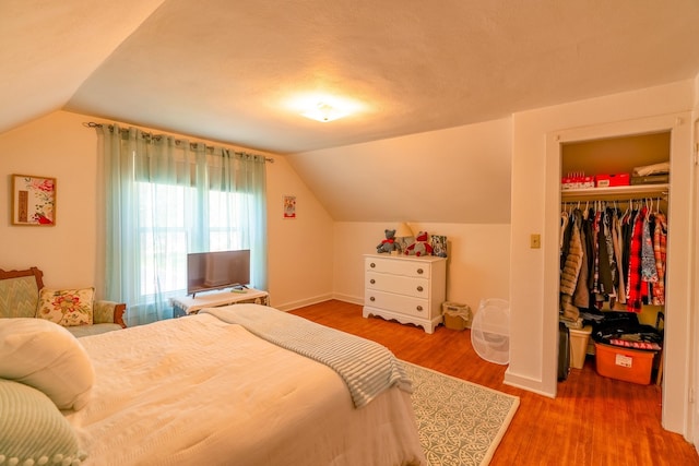 bedroom featuring wood finished floors, lofted ceiling, a closet, a spacious closet, and baseboards