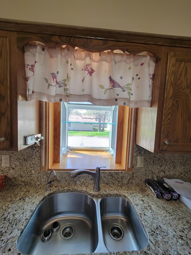 kitchen view of a sink, tasteful backsplash, brown cabinetry, and light stone countertops