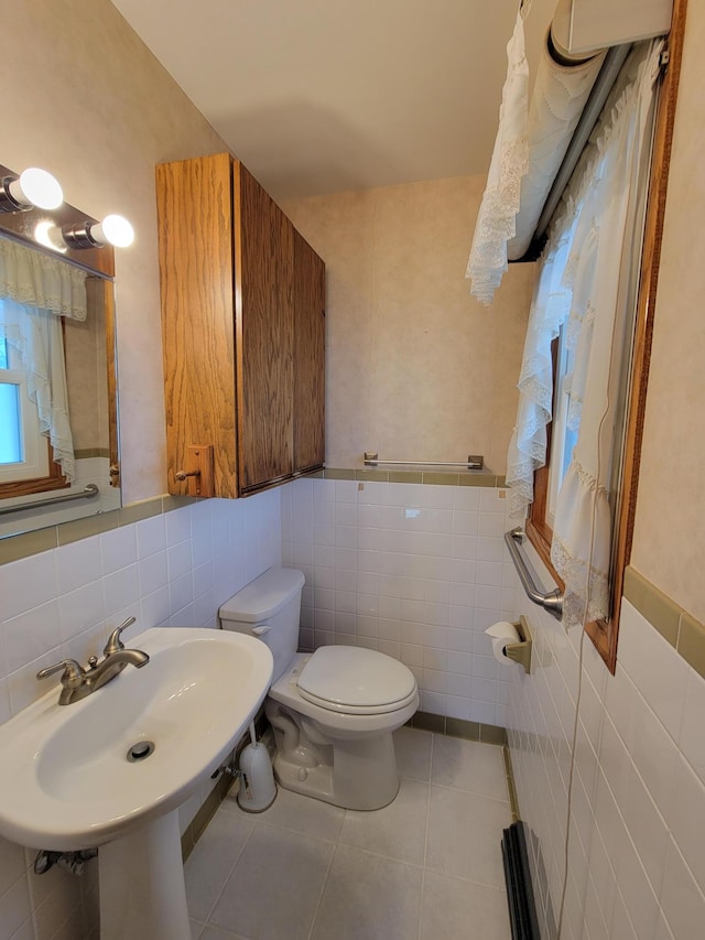 bathroom with tile walls, toilet, tile patterned flooring, a wainscoted wall, and a sink