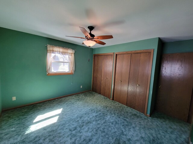 unfurnished bedroom with multiple closets, carpet flooring, a ceiling fan, and baseboards