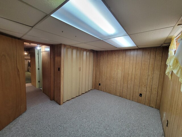 finished below grade area featuring a paneled ceiling, light carpet, and wood walls