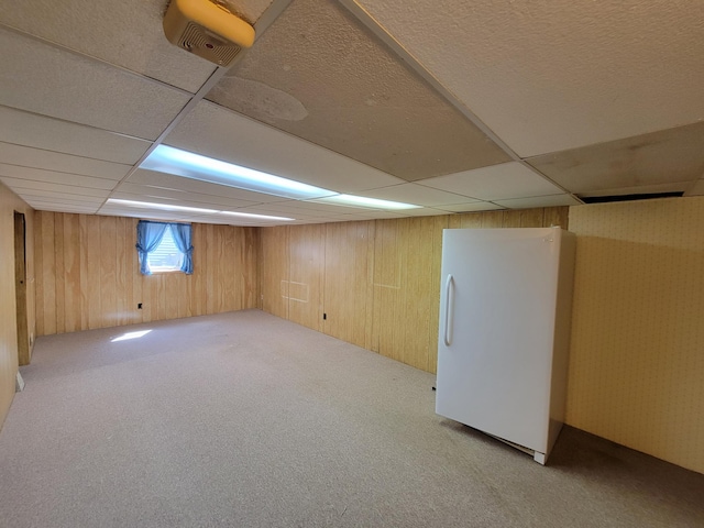 below grade area with freestanding refrigerator, carpet floors, a paneled ceiling, and wooden walls