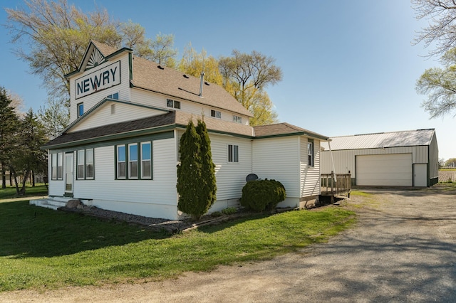view of side of home featuring an outbuilding, a lawn, a garage, and roof with shingles