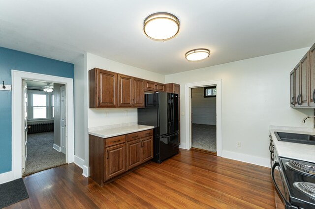 kitchen featuring black appliances, a sink, dark wood-style flooring, light countertops, and baseboards
