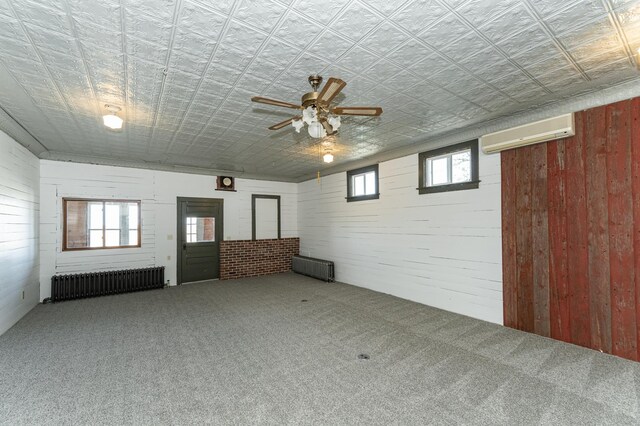 below grade area featuring radiator, wooden walls, a wall mounted AC, carpet floors, and a ceiling fan