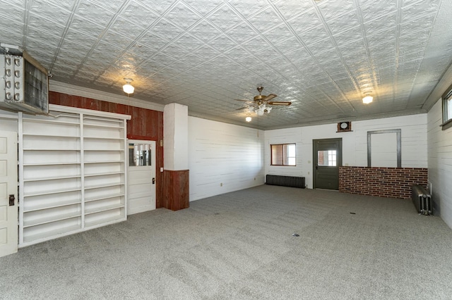 unfurnished living room with carpet, ceiling fan, radiator heating unit, and wooden walls