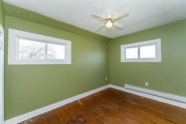empty room with a baseboard heating unit, baseboards, dark wood-type flooring, and ceiling fan