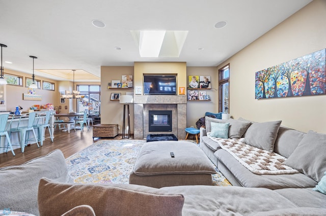 living room with wood finished floors, a skylight, a tiled fireplace, and a chandelier