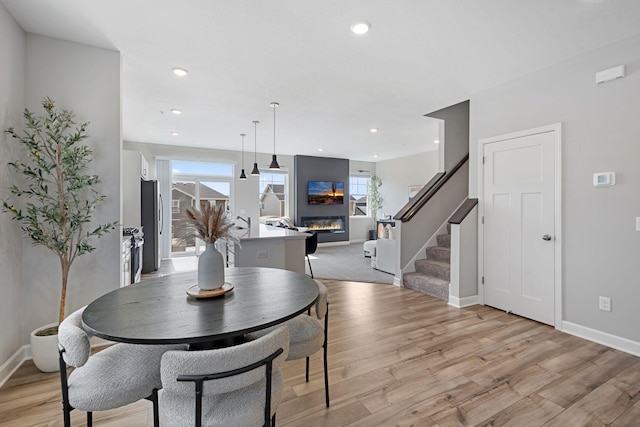 dining space featuring a glass covered fireplace, light wood-style floors, baseboards, stairway, and recessed lighting