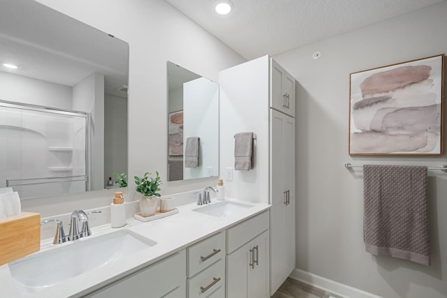 bathroom with double vanity, a shower with shower door, a textured ceiling, recessed lighting, and baseboards