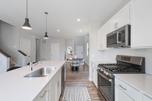 kitchen featuring stainless steel appliances, a sink, light countertops, recessed lighting, and light wood finished floors