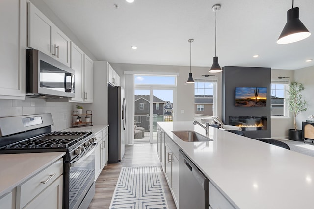 kitchen with appliances with stainless steel finishes, a sink, light countertops, a glass covered fireplace, and recessed lighting