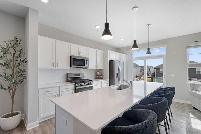 kitchen featuring appliances with stainless steel finishes, a sink, light wood-style floors, backsplash, and baseboards