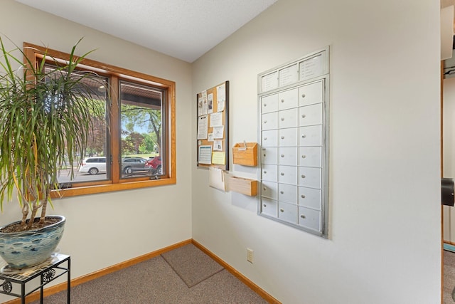 hallway with carpet flooring, baseboards, and mail area