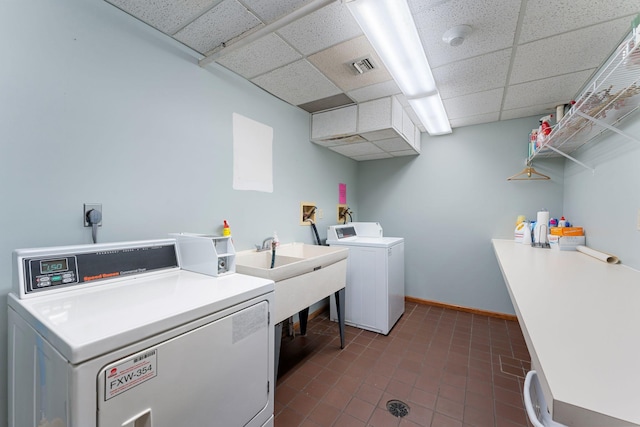 clothes washing area with washing machine and clothes dryer, dark tile patterned floors, baseboards, and a sink