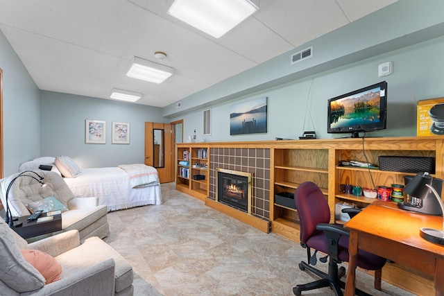 bedroom featuring an office area and a tile fireplace