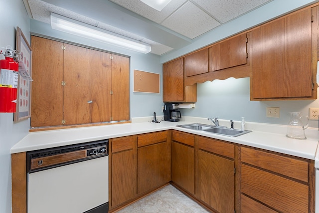 kitchen featuring dishwasher, a sink, a drop ceiling, light countertops, and brown cabinetry