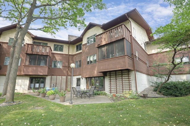back of property featuring a patio, a lawn, a balcony, and stucco siding