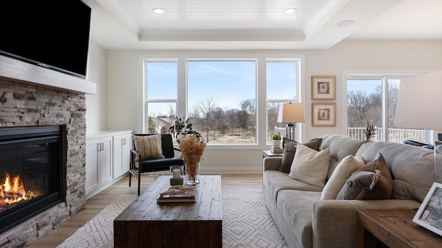 living area featuring a tray ceiling, a stone fireplace, light wood-type flooring, recessed lighting, and ornamental molding