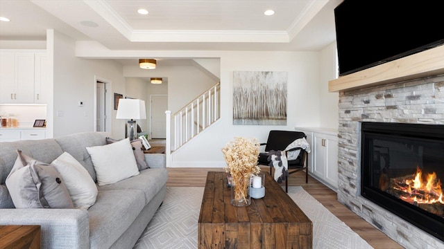 living area with a raised ceiling, stairs, light wood-style floors, a fireplace, and recessed lighting