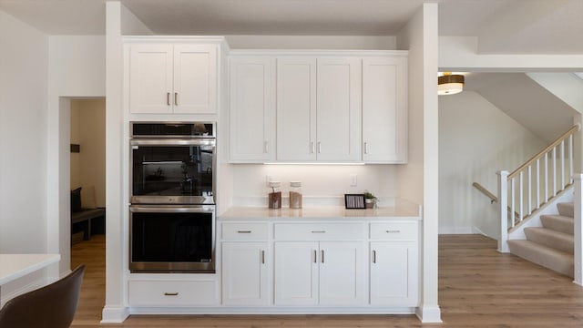 kitchen with stainless steel double oven, light wood finished floors, white cabinets, and light countertops