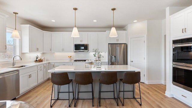kitchen featuring appliances with stainless steel finishes, a sink, a kitchen island, a kitchen breakfast bar, and white cabinets