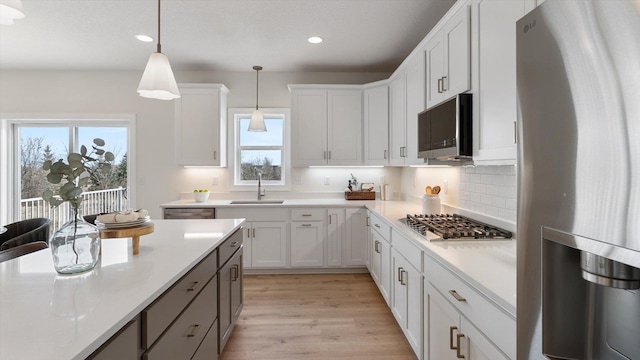 kitchen featuring stainless steel appliances, a sink, recessed lighting, light countertops, and pendant lighting