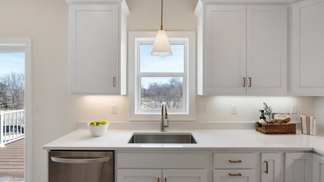 kitchen featuring stainless steel dishwasher, a sink, light countertops, white cabinets, and decorative light fixtures