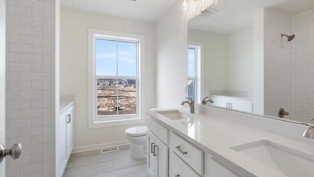 bathroom with a shower, double vanity, and toilet