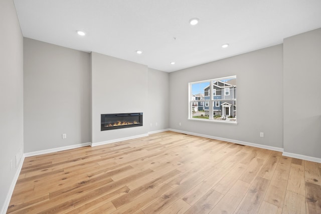 6750 Wildflower Way, Minnetrista, MN 55331 - unfurnished living room featuring light wood-type flooring, baseboards, a glass covered fireplace, and recessed lighting