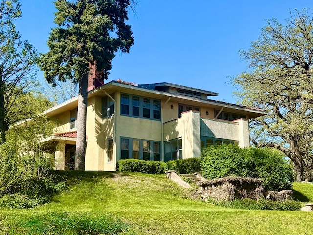 rear view of house featuring stucco siding, a chimney, and a yard