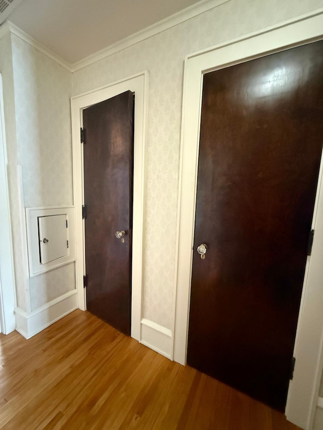 hallway with wood finished floors, crown molding, and wallpapered walls