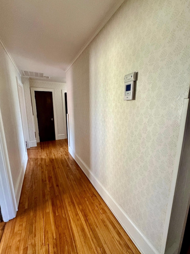 hallway featuring ornamental molding, wood-type flooring, and baseboards