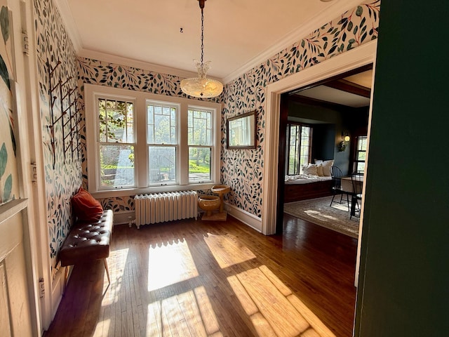 dining area featuring radiator, wallpapered walls, crown molding, wood-type flooring, and baseboards