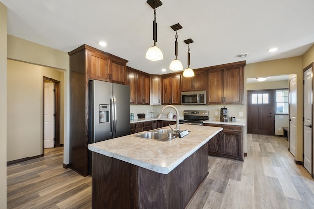 kitchen featuring stainless steel appliances, a sink, light countertops, light wood-type flooring, and decorative light fixtures
