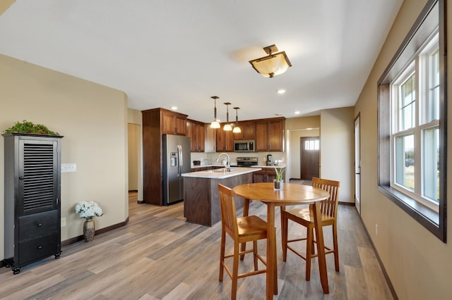 kitchen with light wood-style flooring, a sink, stainless steel appliances, a kitchen island with sink, and light countertops