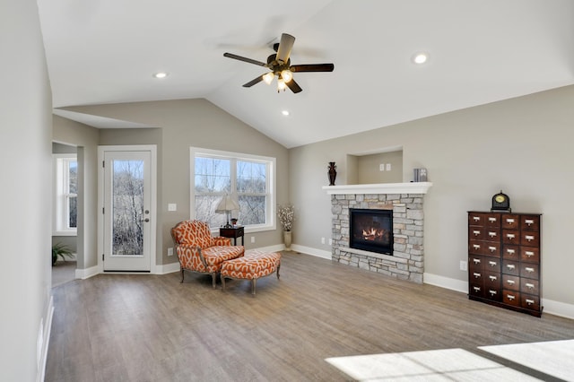 living area with ceiling fan, a stone fireplace, lofted ceiling, wood finished floors, and baseboards