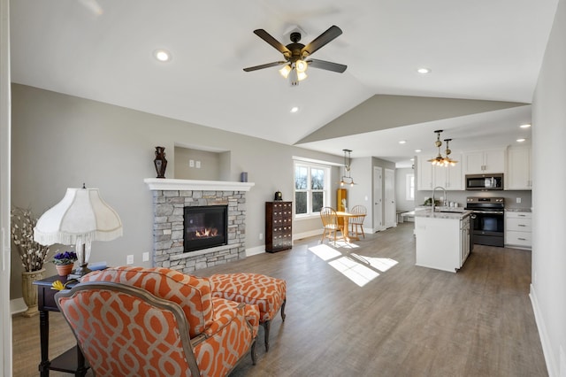 living area featuring vaulted ceiling, baseboards, ceiling fan, wood finished floors, and a fireplace