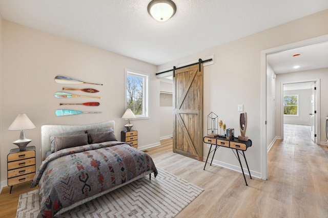 bedroom featuring a barn door, light wood finished floors, and baseboards