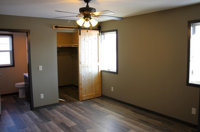 unfurnished bedroom featuring a barn door, dark wood finished floors, and baseboards