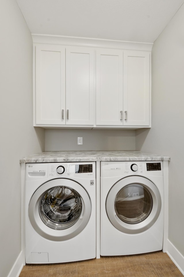 washroom featuring washing machine and dryer, light wood-style flooring, cabinet space, and baseboards