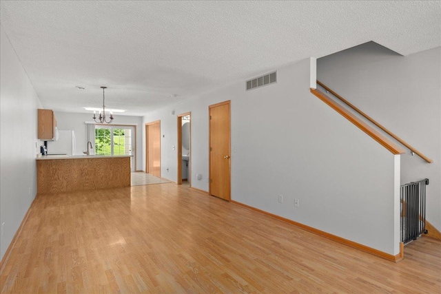 1960 Pika Trl Unit C, River Falls, WI 54022 - unfurnished living room with light wood-style flooring, a chandelier, a textured ceiling, a sink, and baseboards