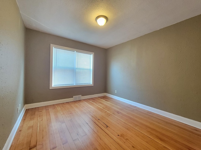 unfurnished room with visible vents, baseboards, hardwood / wood-style floors, and a textured wall