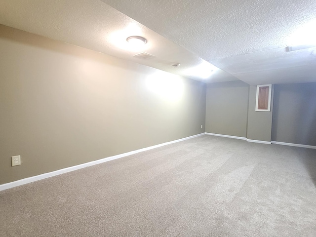 finished basement featuring a textured ceiling, light carpet, and baseboards