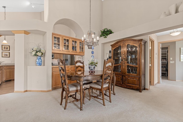 dining area featuring light carpet, a chandelier, a high ceiling, and baseboards