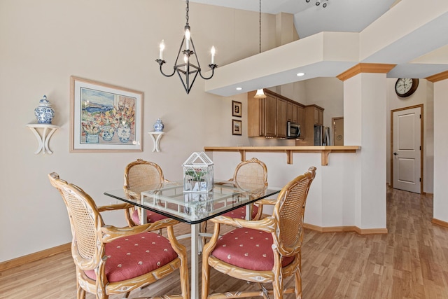 dining space featuring a chandelier, high vaulted ceiling, light wood-type flooring, and baseboards