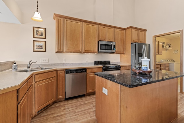 kitchen with appliances with stainless steel finishes, a sink, washer and clothes dryer, a high ceiling, and light wood-style flooring
