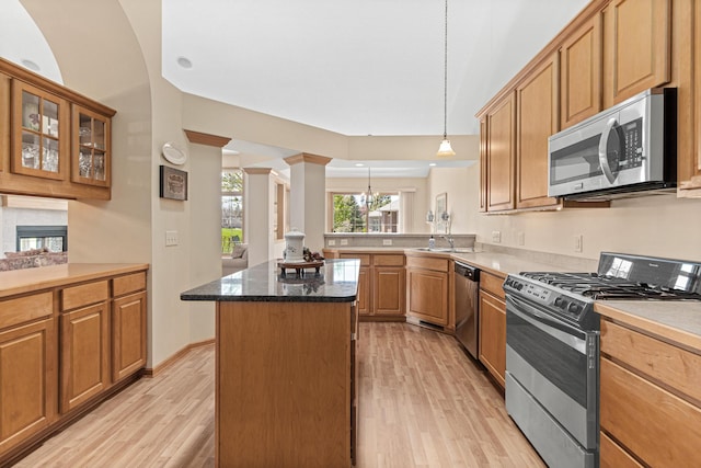 kitchen with appliances with stainless steel finishes, light wood-style floors, a center island, glass insert cabinets, and pendant lighting