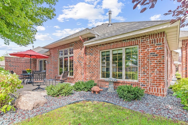 back of property featuring brick siding, a patio, and roof with shingles